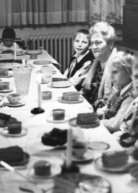 Ältere Dame zwischen Kindern an Kaffeetafel