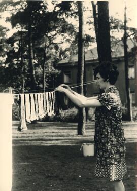 Frau in Kittelschürze beim Aufhängen von Wäsche